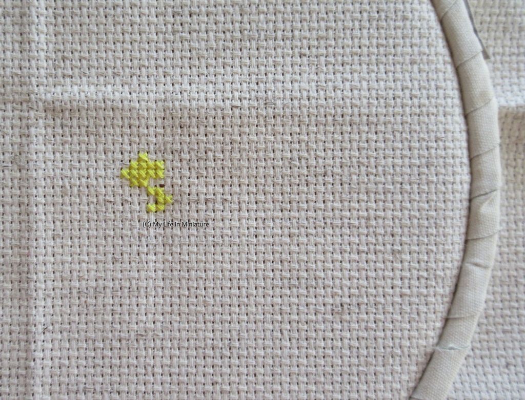 A very small amount of lemon yellow cross-stitching has been done on cream fabric. 