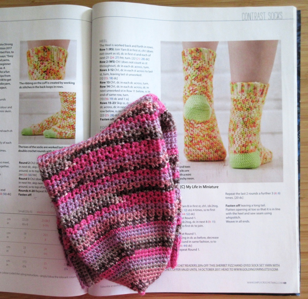 The socks, stacked and folded in half, sit on an open magazine. The magazine is open to the sock pattern, and images of the model socks are clearly visible.