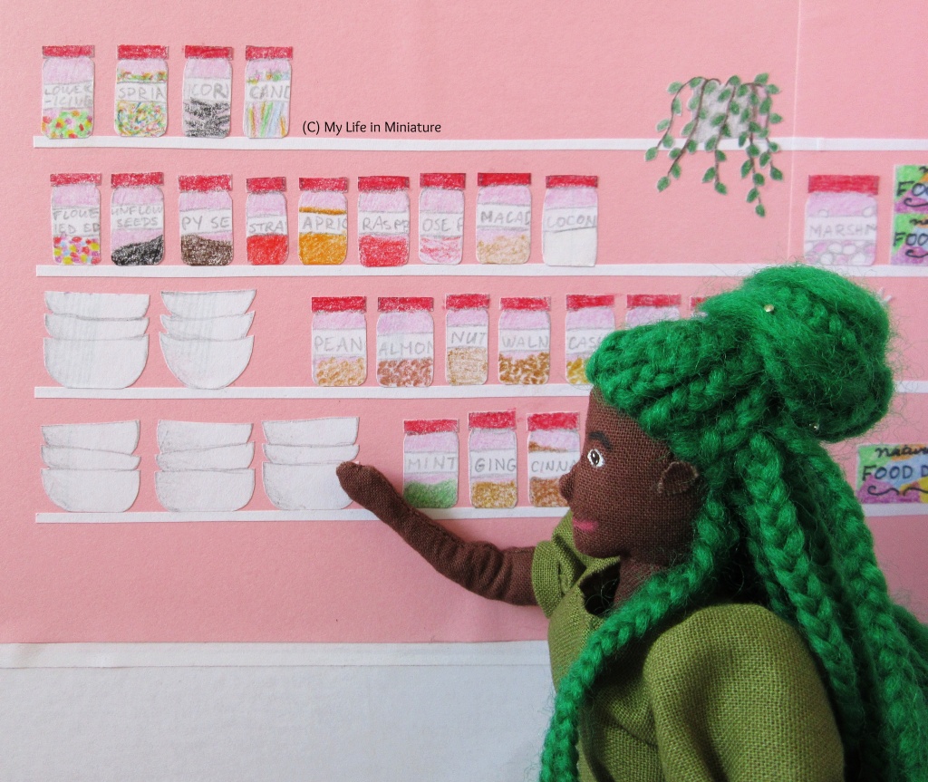 Close-up of one side of the shelves in Fierro's back room. Hazel is reaching for a bowl from one of the stacks, wearing a green puffy-sleeved dress and with her green braids in a bun. The labels on the jars are more clear now; the ones on the top shelves contain things like marshmallows, jams, seeds, sprinkles, candles, and shredded coconut.