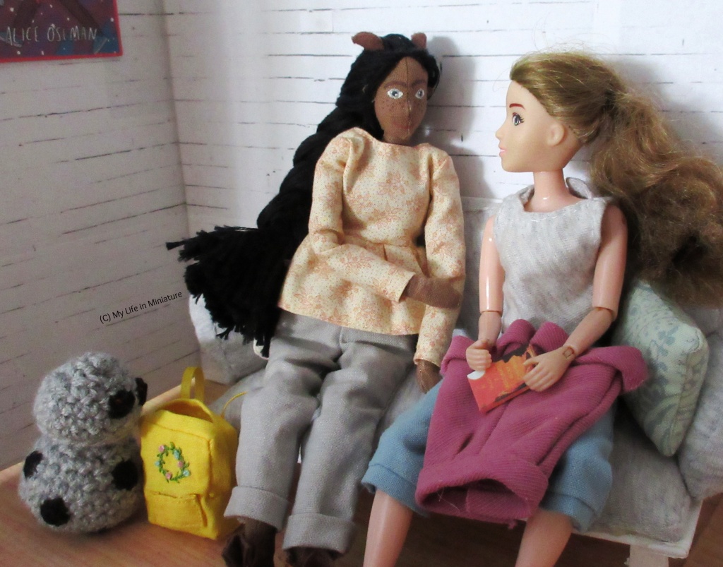 Sarah and Petra sit on Sarah's couch. Sarah has the pink corduroy shorts and the book in her lap, and is thanking Petra. Petra is beside her, smiling at her. In the corner, Chip is investigating Petra's bag. 
