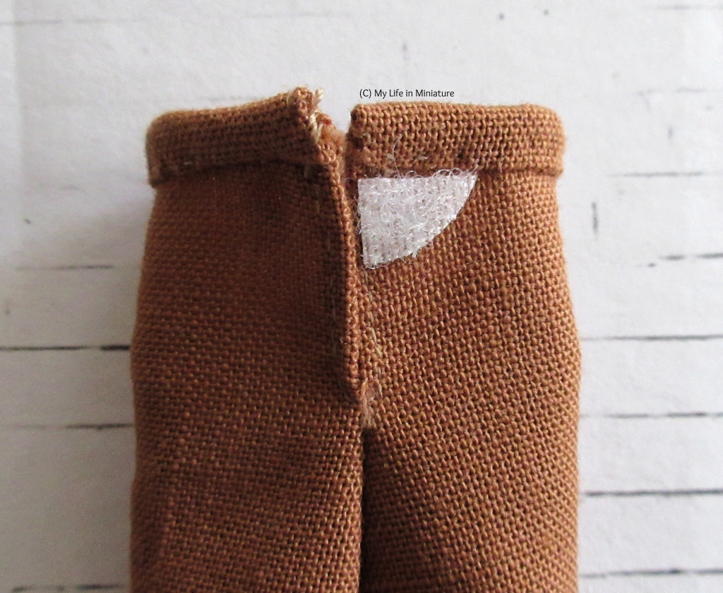 Close-up of the back closure of the brown pants. The pants close with a small patch of velcro just under the waistband. 